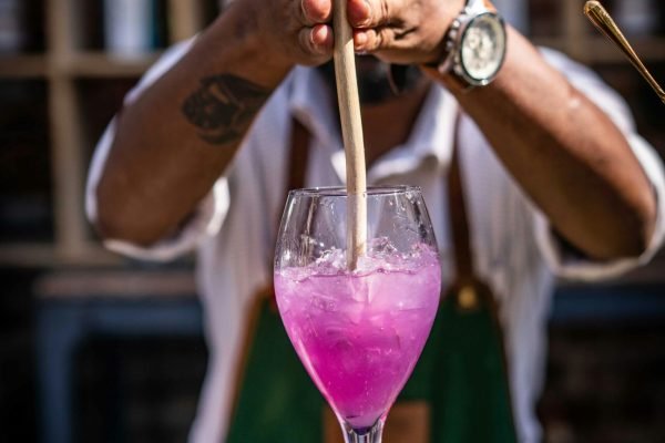 Bartender skillfully mixes a vibrant purple cocktail at an indoor bar setting.