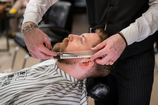 A skilled barber meticulously trims a client's beard using comb and scissors in a modern barbershop.